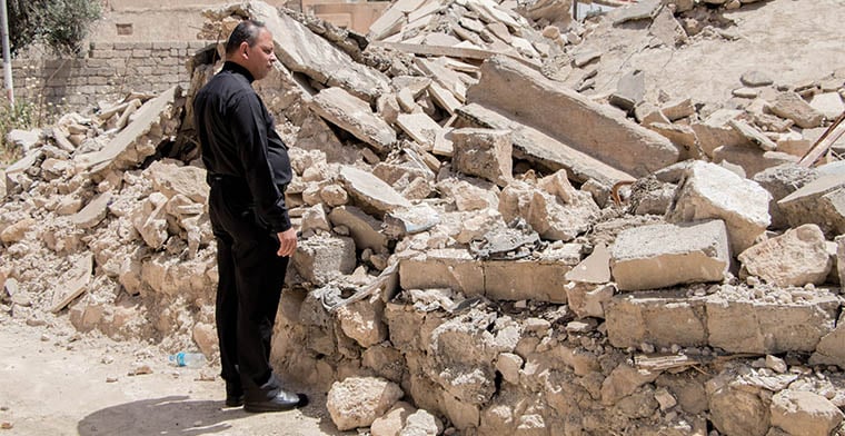 A priest looks at his childhood home in ruins, in Iraq