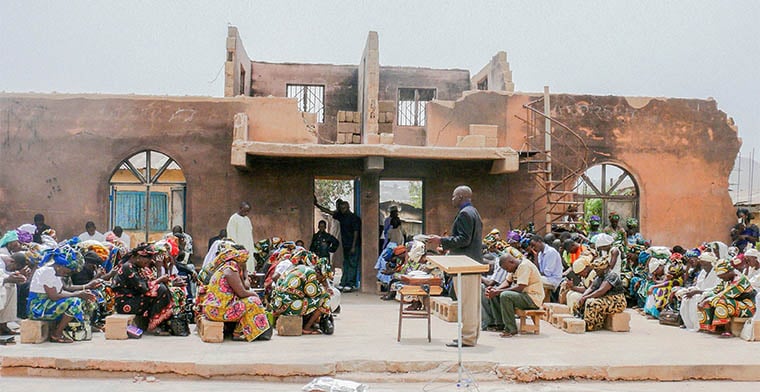 A congregation in Nigeria holds a church service in the open air in front of what was once their church, now destroyed.