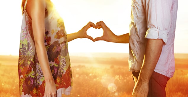 Couple in sunset with hands forming a heart 