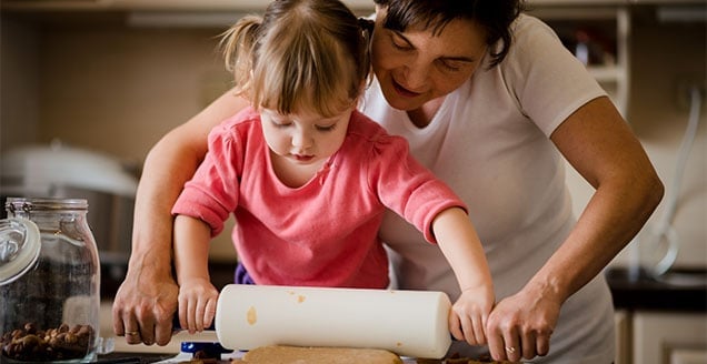 Mother and child preparing dough with rolling pin in kitchen at home
