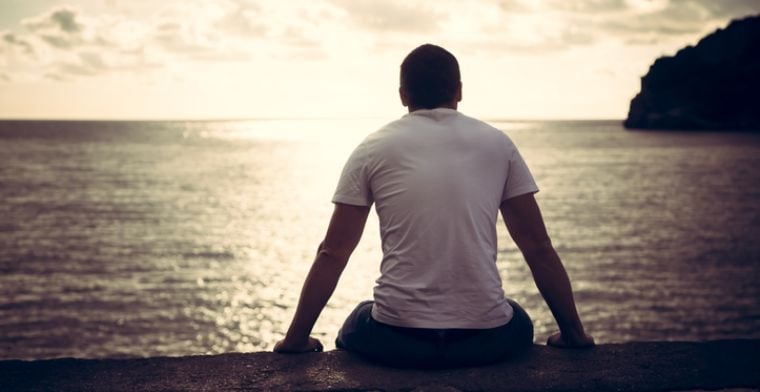Man sitting on shore looking out to horizon
