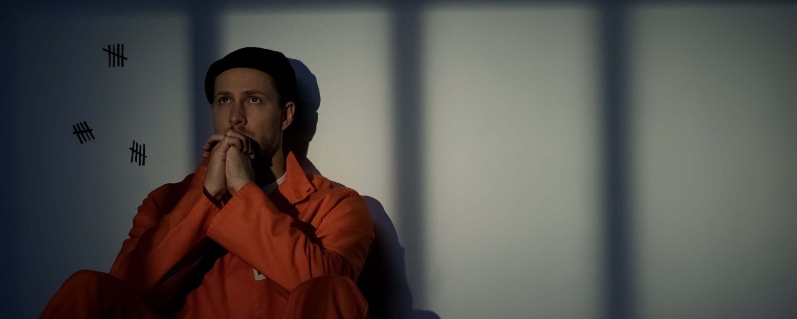 Caucasian male prisoner praying, feeling guilty about crimes, asking for mercy