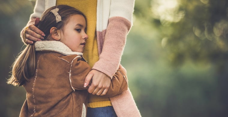 Sad girl feeling protected in her mother's embrace outdoors.