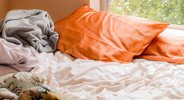 Messy unmade bed with bright orange pillows