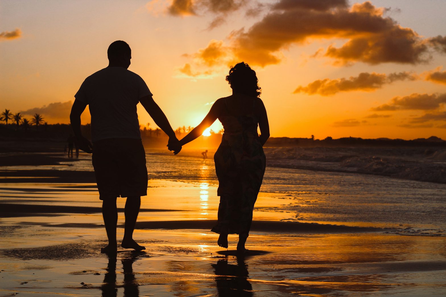 Couple holding hands on a beach at sunrise or sunset